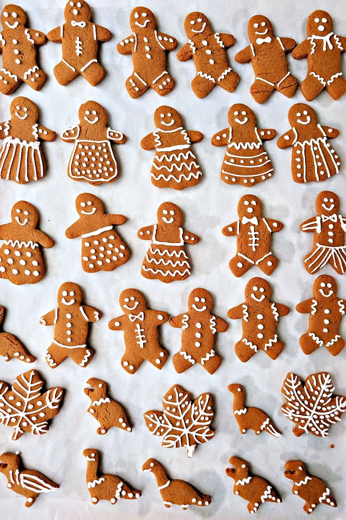 Gingerbread people and dinosaur cookies decorated with white royal icing on parchment paper
