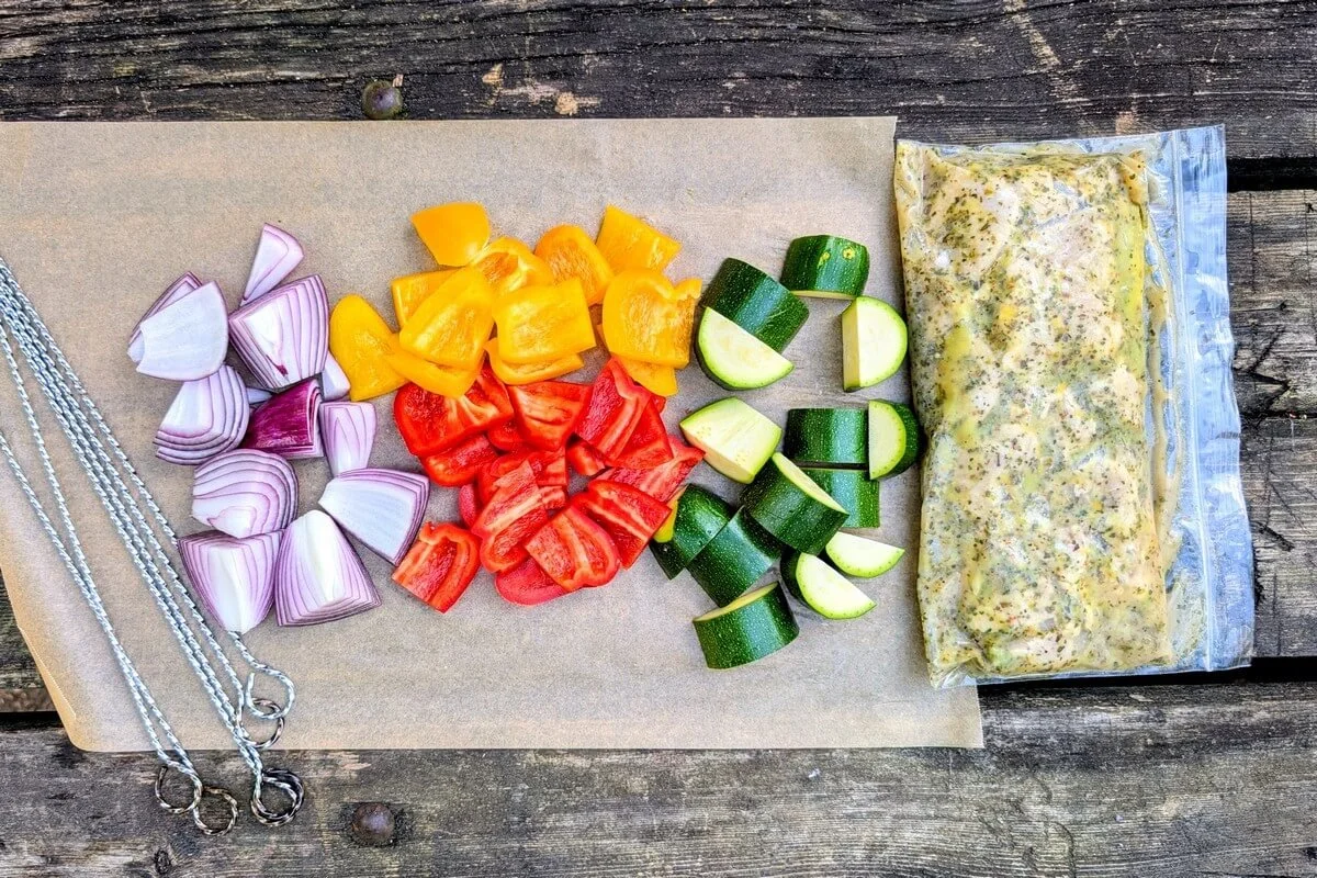Prepped vegetables and marinated chicken in a zip-top bag for camping chicken skewers on a picnic table