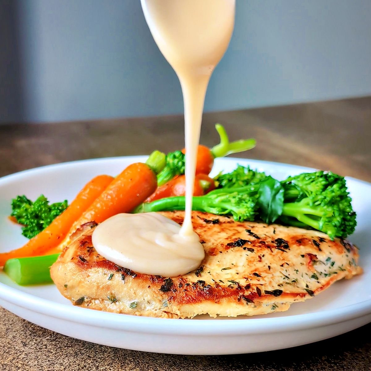 Homemade velouté sauce poured over pan-seared chicken breast with broccolini and carrots