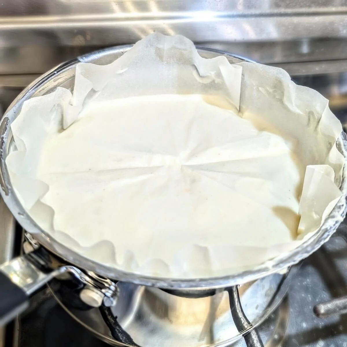 Bechamel sauce in a saucepan with parchment paper pressed directly onto its surface to prevent a skin from forming