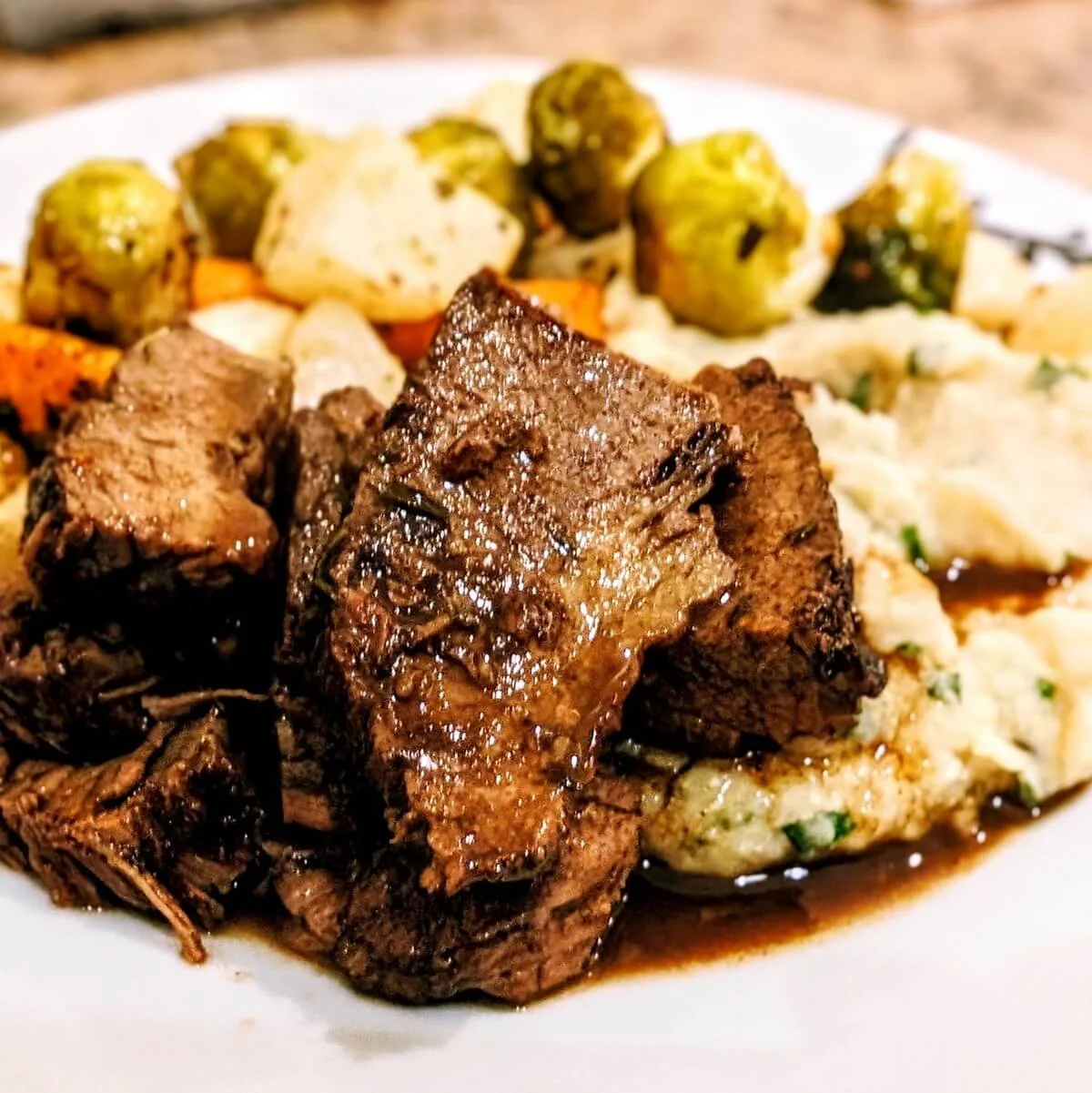 Sliced beef brisket served with red wine jus on a plate with cauliflower mash and veggies for Christmas dinner