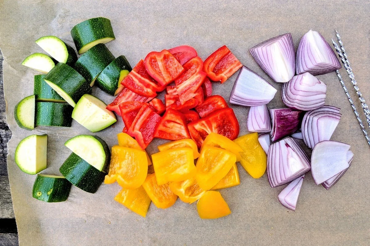 Close-up of evenly cut zucchini, bell peppers, and red onion pieces prepared for chicken skewers over a campfire