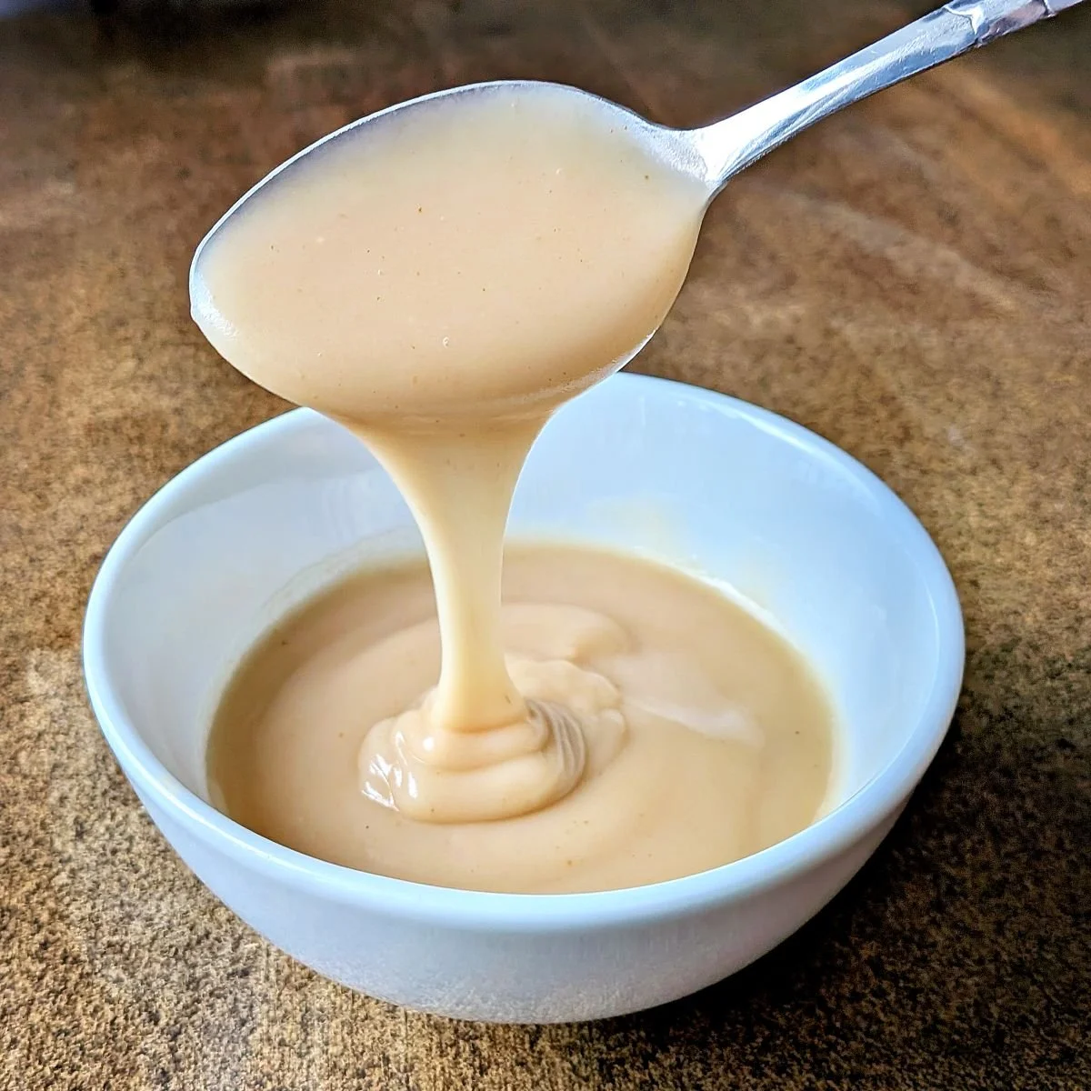 Velouté sauce drizzling from a spoon into a white bowl