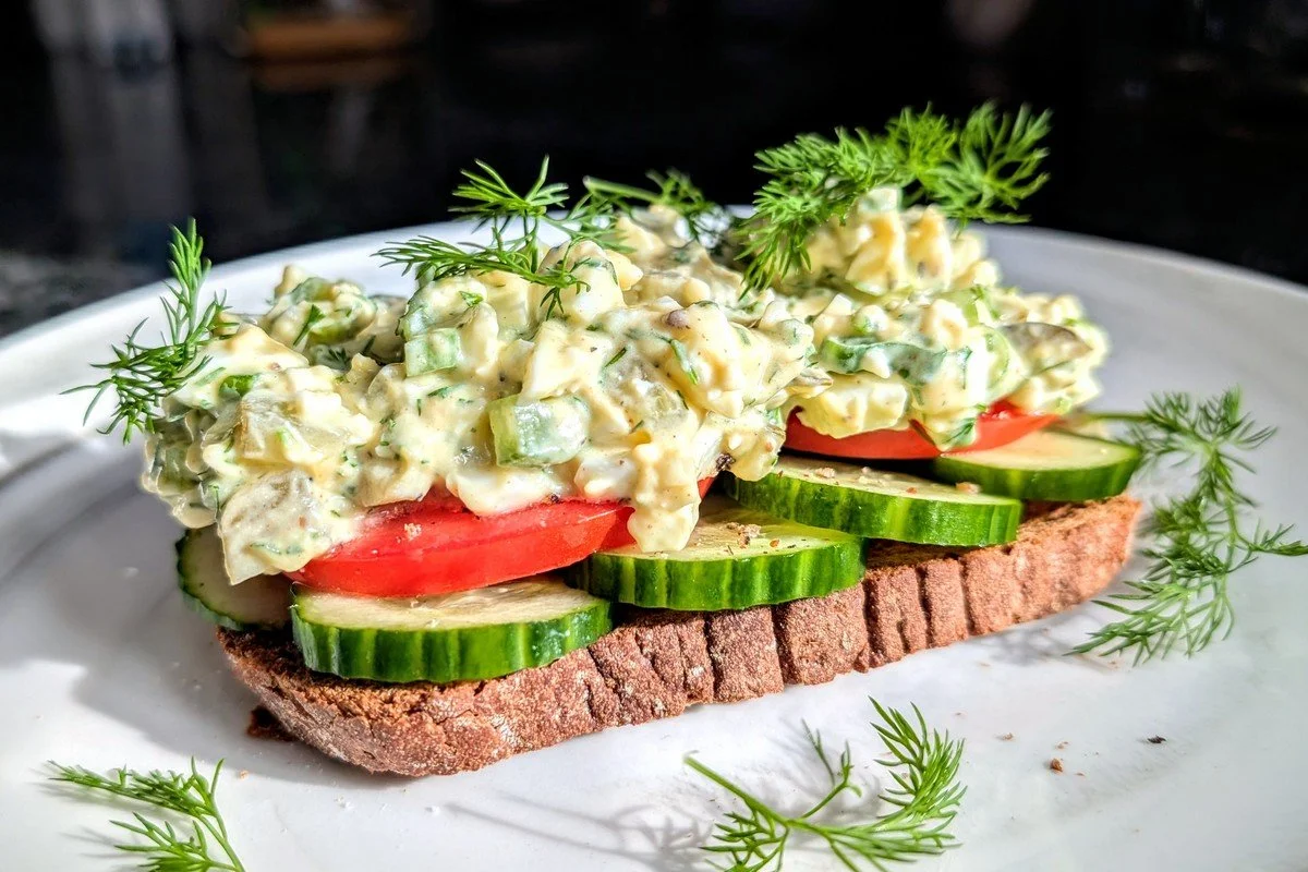 No mayo egg salad on a piece of toast with cucumber, tomato, and fresh dill