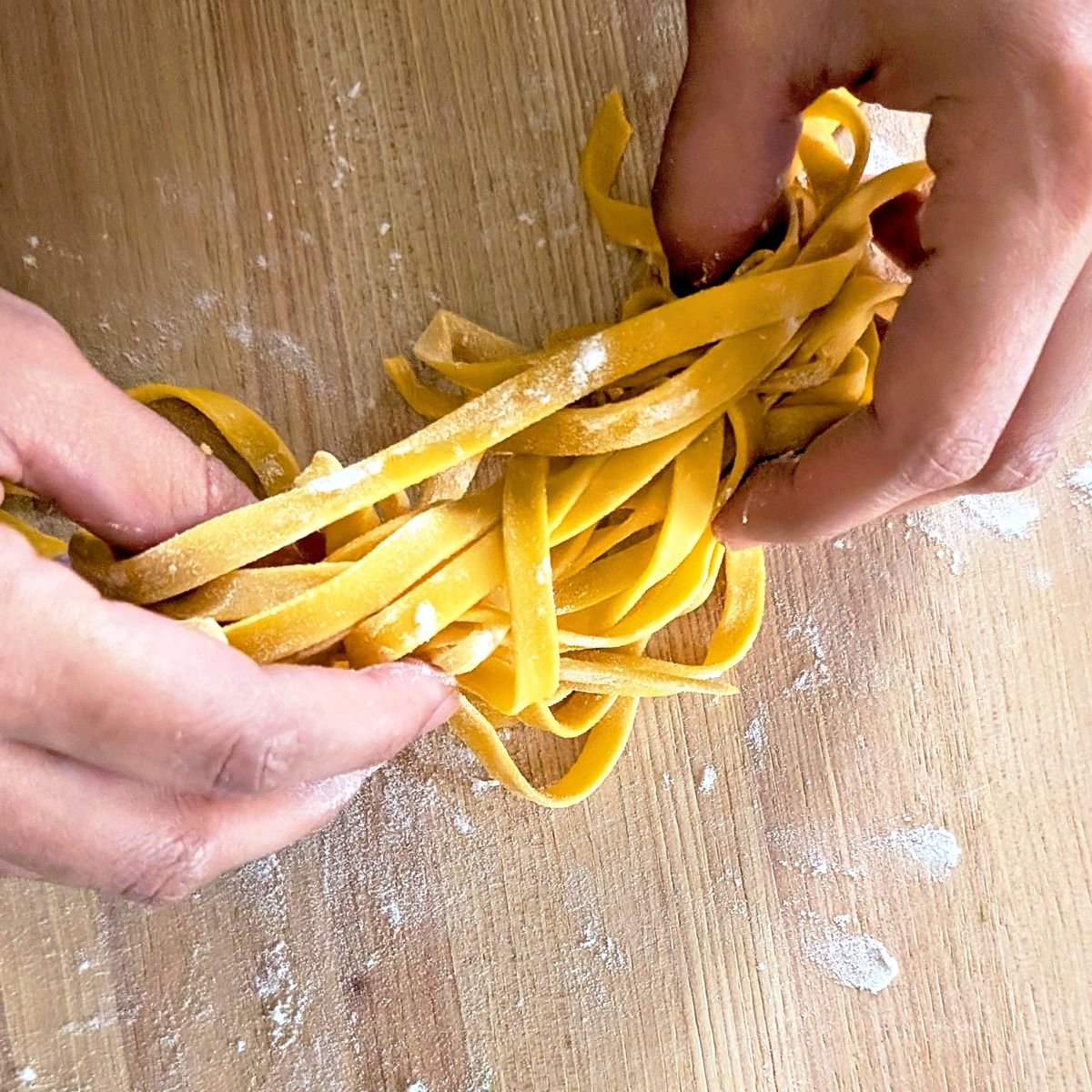 Fresh cut egg pasta noodles being tossed with flour on a wooden cutting board