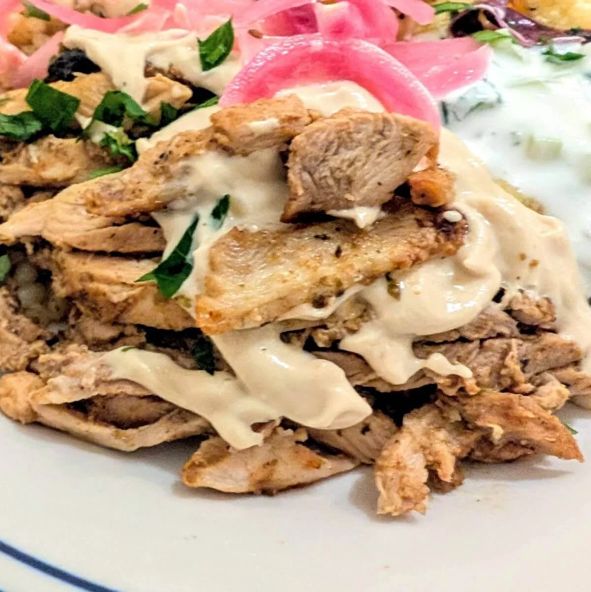 Tahini sauce for shawarma on a plate with homemade chicken shawarma, pickled onions, and herbs
