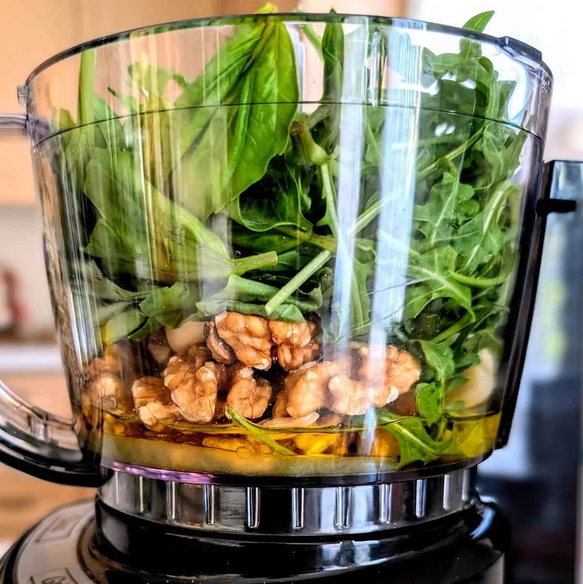 Food processor filled with baby arugula, basil, walnuts, lemon juice, cheese, garlic, and olive oil for arugula basil walnut pesto recipe