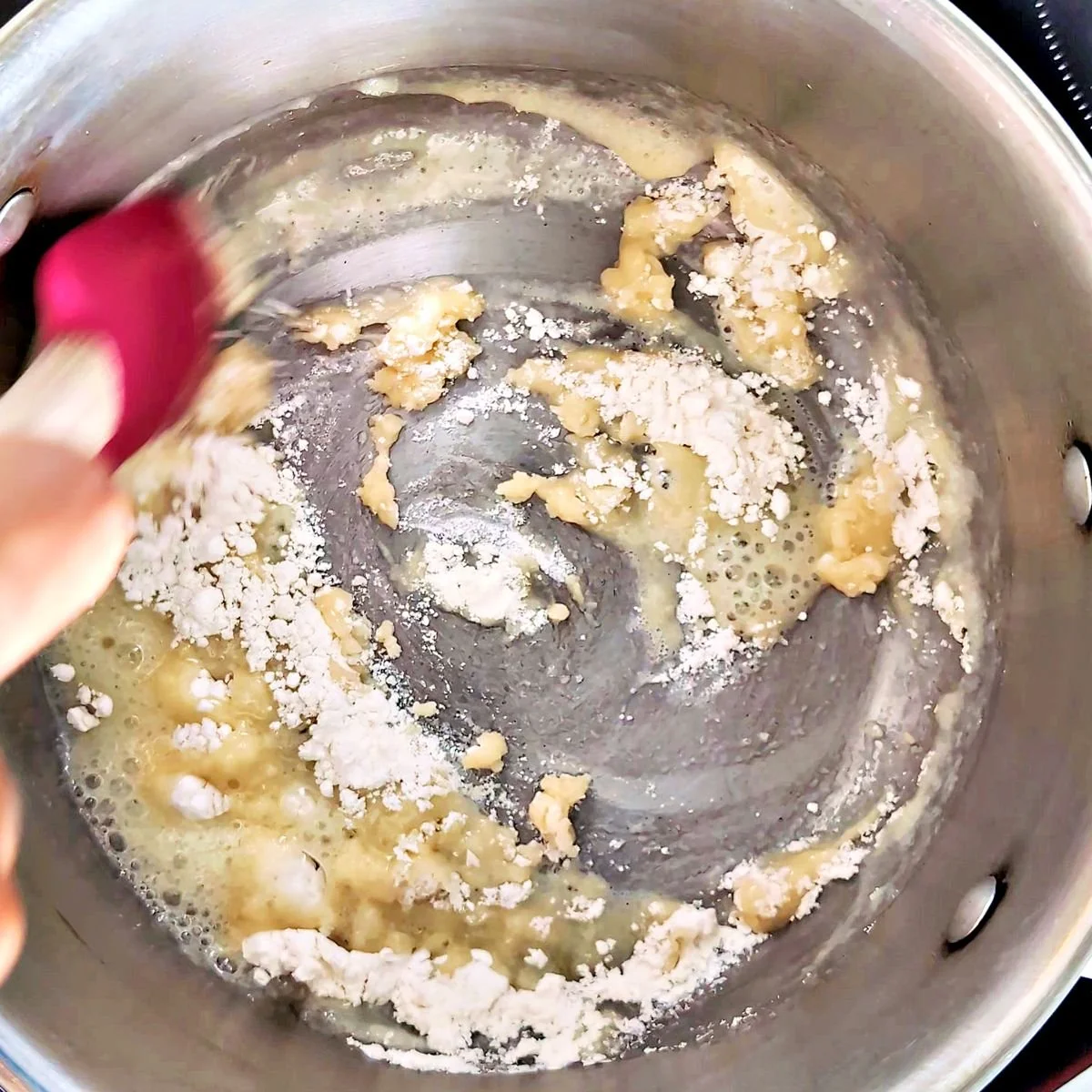 Flour and butter being stirred together in a pan to make roux