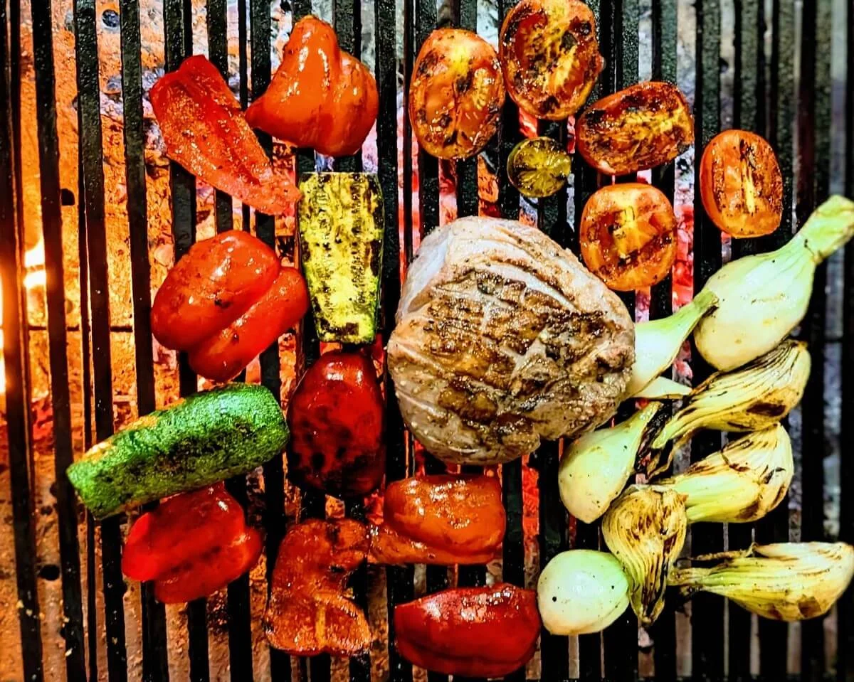 Lamb leg roast with summer vegetables and charred limes cooking on a grill