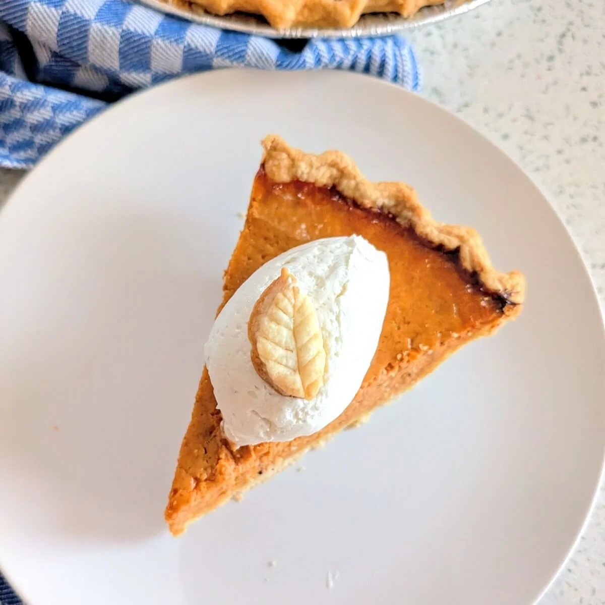 Homemade pumpkin pie slice with flaky all-butter crust, with homemade whipped cream on top ready to eat
