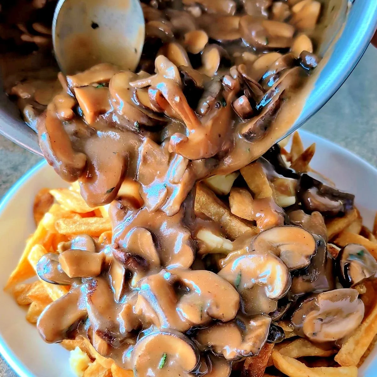 Mushroom gravy being spooned over crispy fries to make poutine