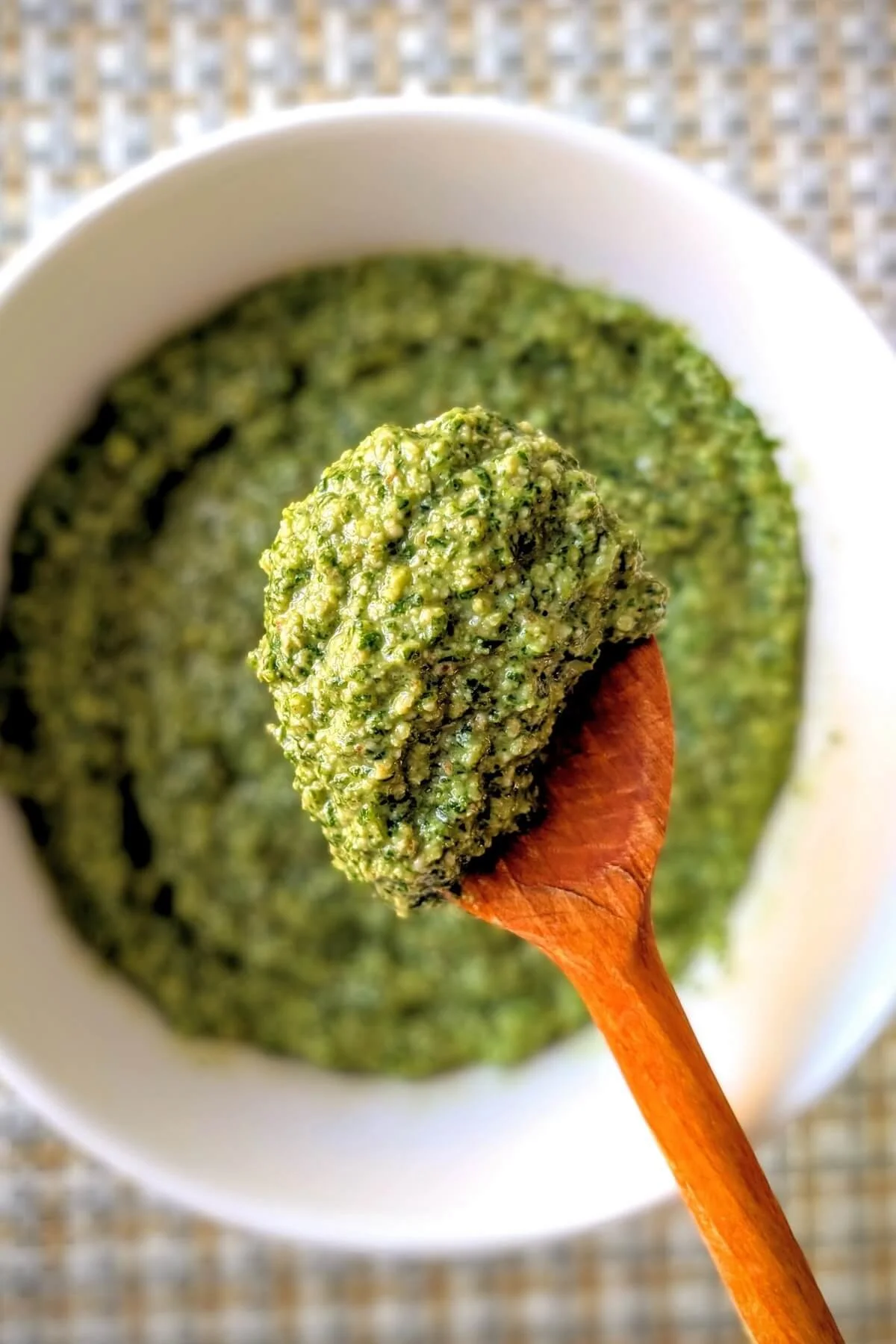 Arugula basil walnut pesto recipe on wooden spoon above white bowl with thick texture and bright green color