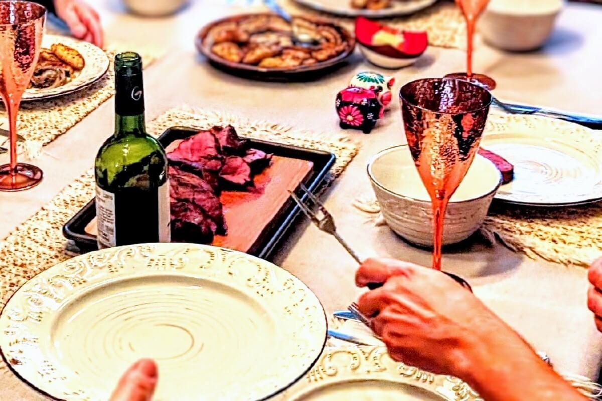 A holiday dinner table with food, plates, drinks, and hands passing food
