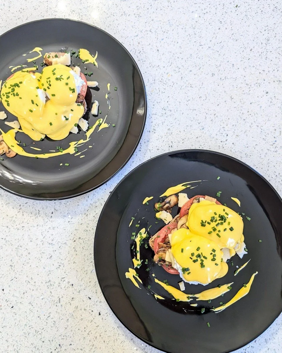 Easy immersion blender hollandaise mother sauce draped over eggs benedict, served on two black plates