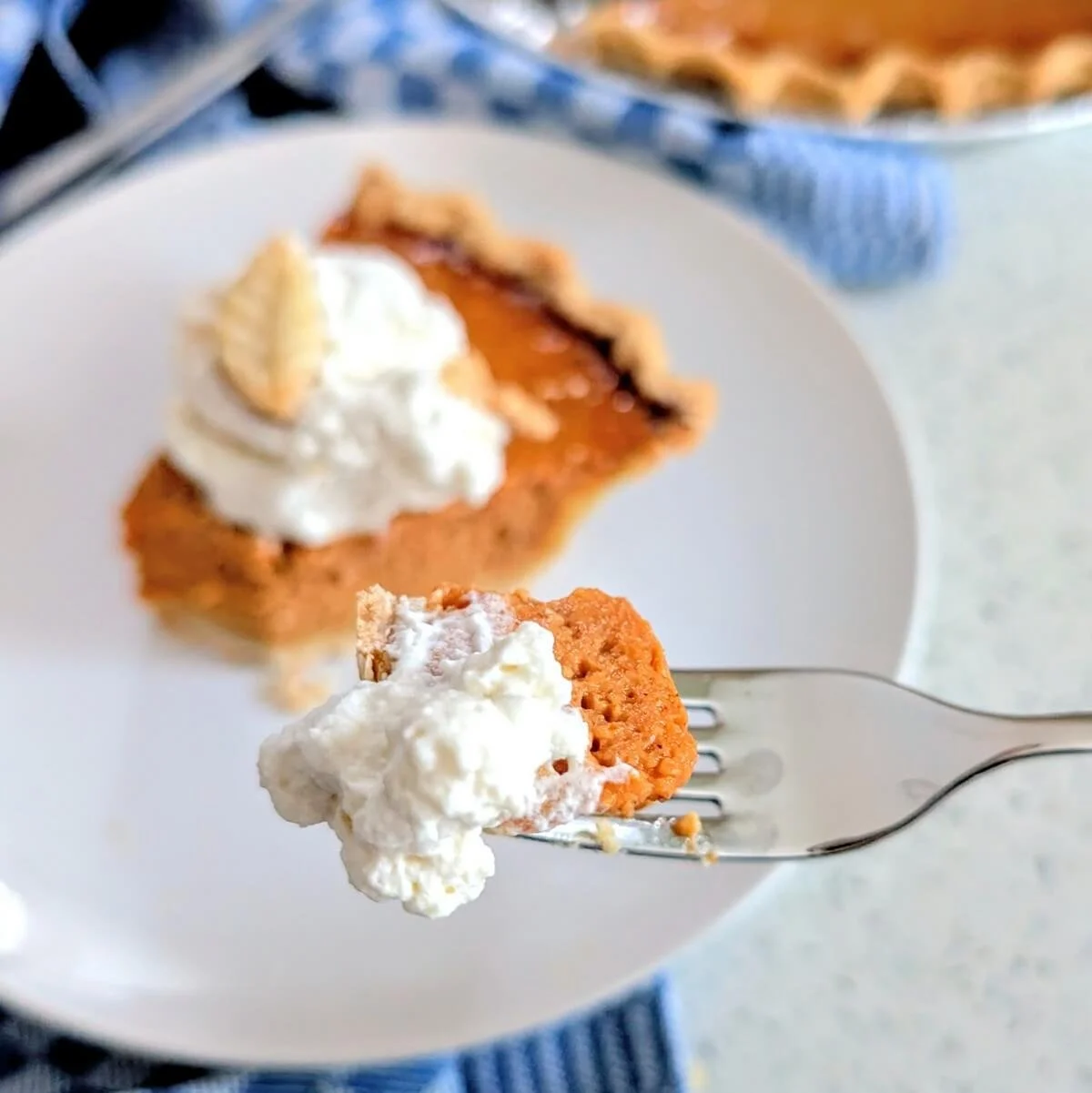 A bite of homemade pumpkin pie with homemade pie crust on a fork with whipped cream
