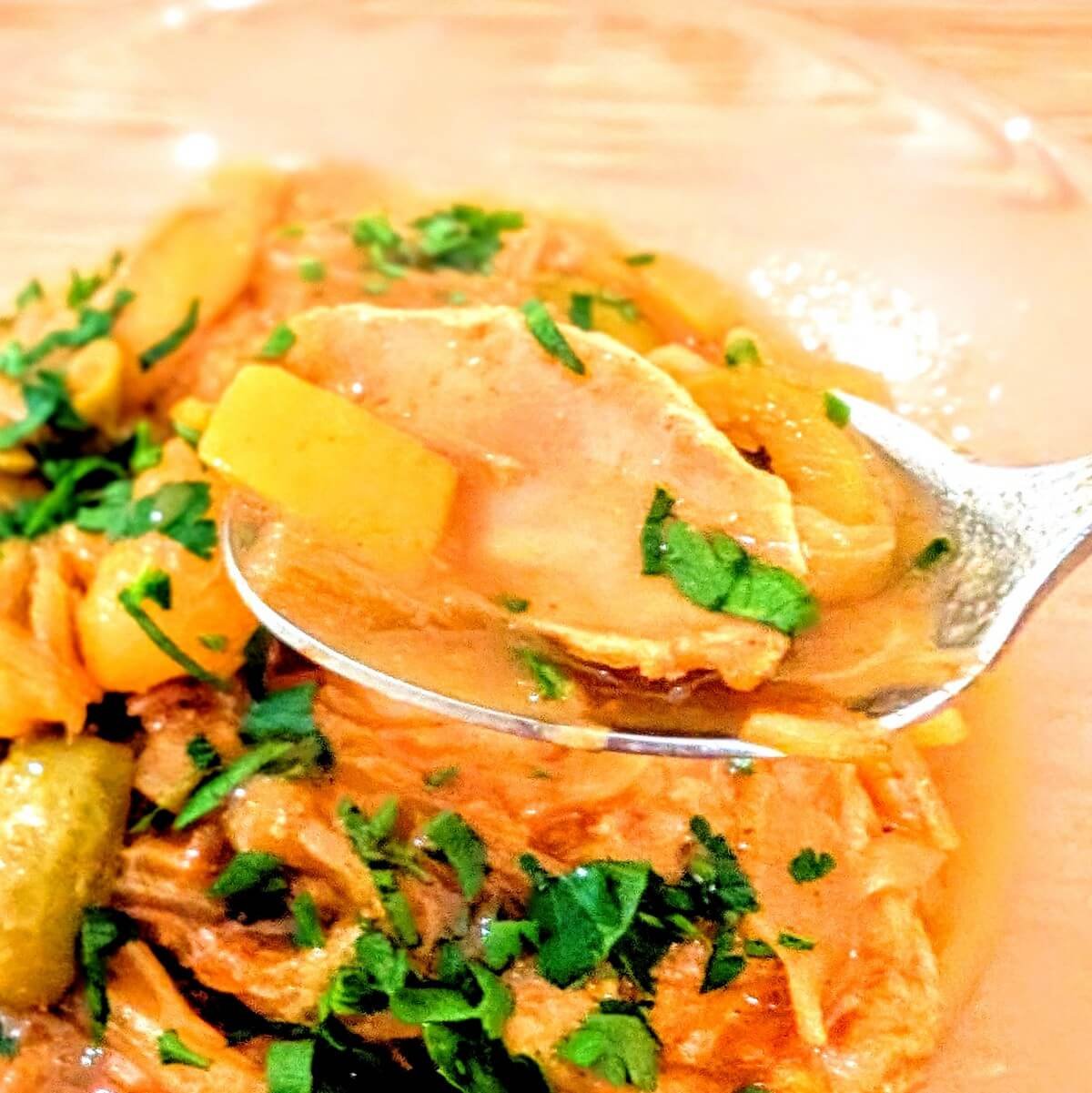 A spoonful of chicken and olive tagine with preserved lemon and apricots held over a bowl of Moroccan chicken tagine