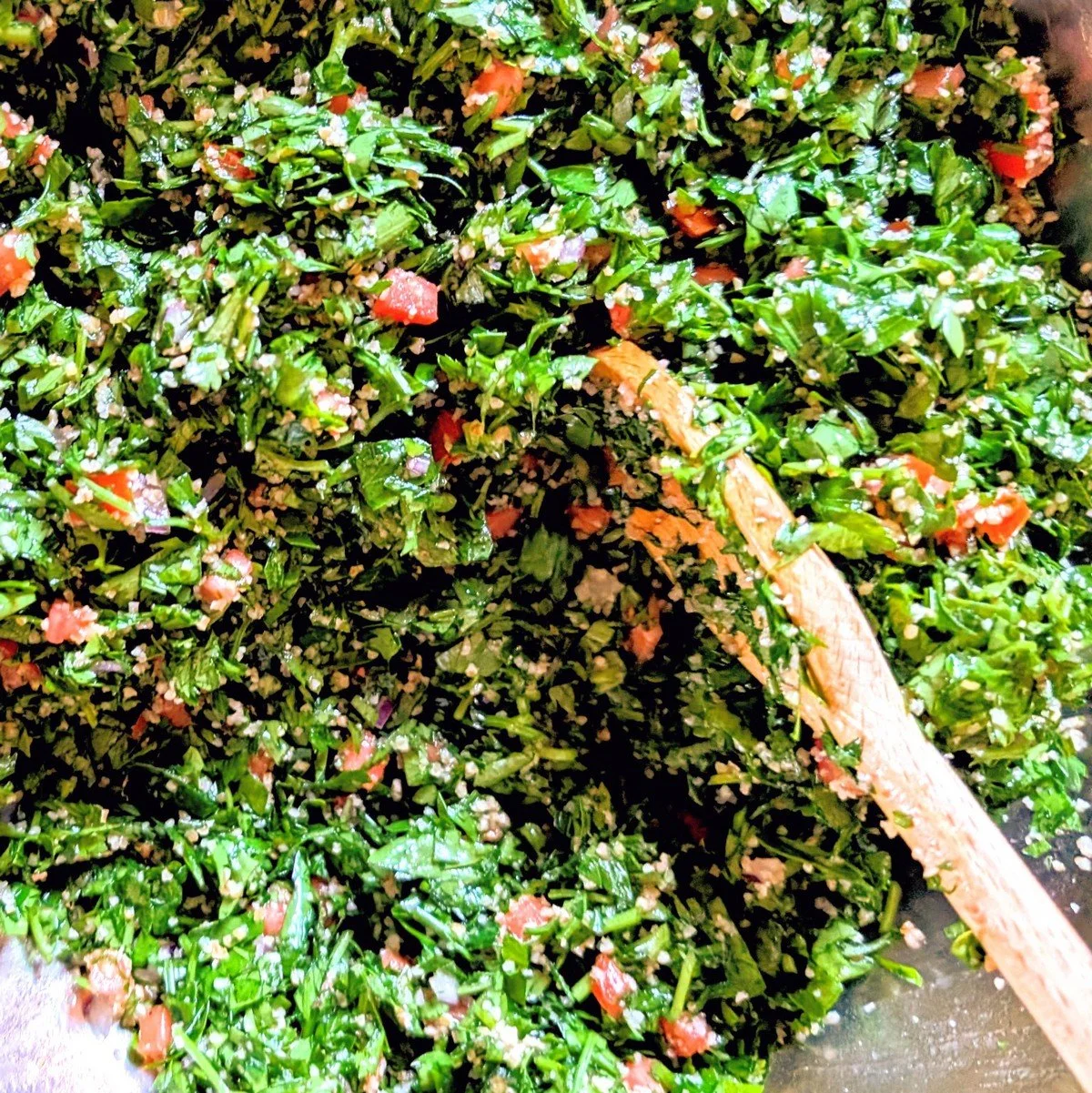 Tabbouleh salad being mixed in a bowl with flat-leaf parsley, soaked fine bulgur, tomato, green onion, lemon juice, and olive oil