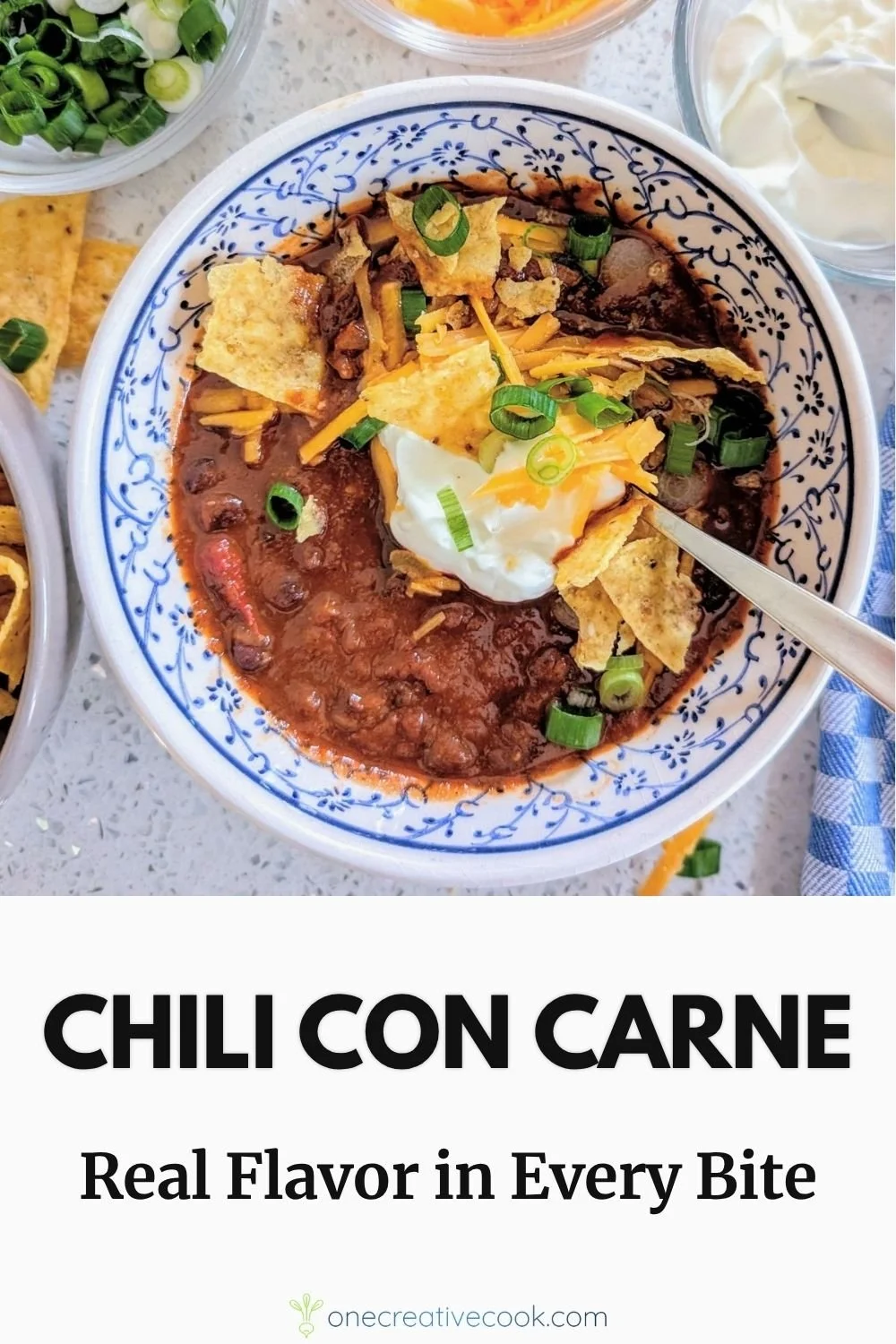 Bowl of chunky beef chili with black beans, cheddar cheese, sour cream, and fresh scallions, served with tortilla chips