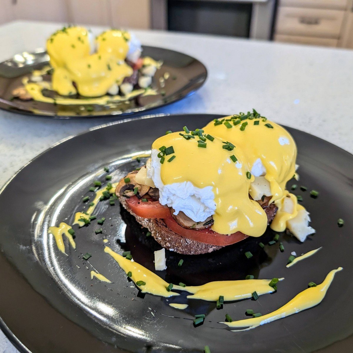 Immersion blender hollandaise sauce spooned over poached eggs on toast with tomatoes, mushrooms, cheese, and chives