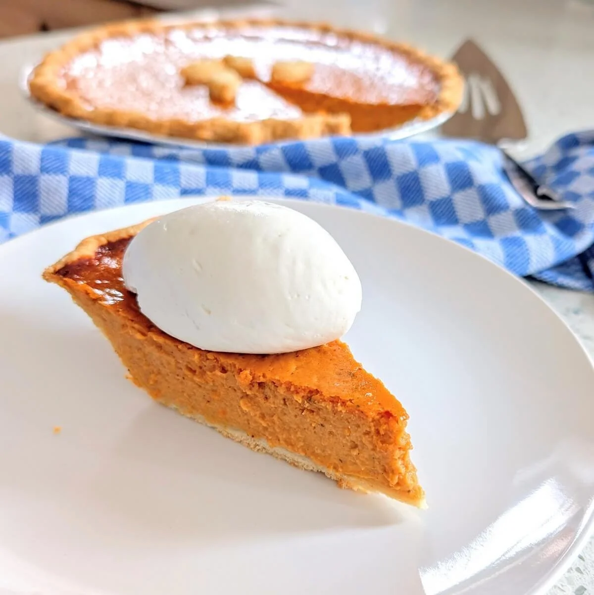 Homemade pumpkin pie slice on a plate with a quenelle of whipped cream on top