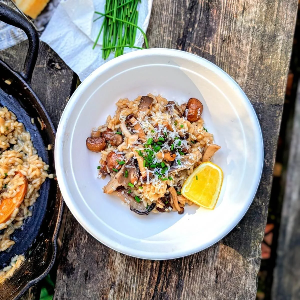 Creamy mushroom risotto served in a paper bowl with lemon wedge on a camp table