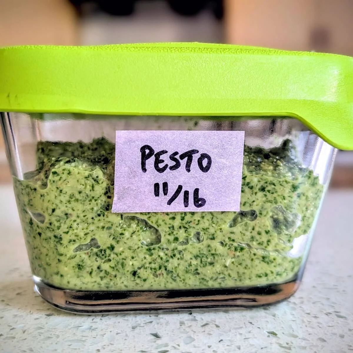 Homemade arugula basil walnut pesto stored in glass container with green lid and label