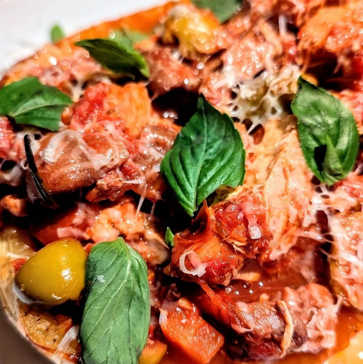 Close-up of turkey cacciatore served over roasted spaghetti squash, topped with olives, fresh basil, braised turkey chunks, parmesan, and rustic tomato sauce