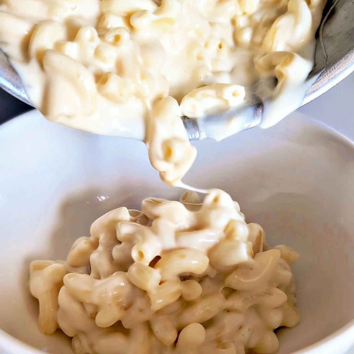 Creamy mornay sauce coated mac and cheese being served into a bowl
