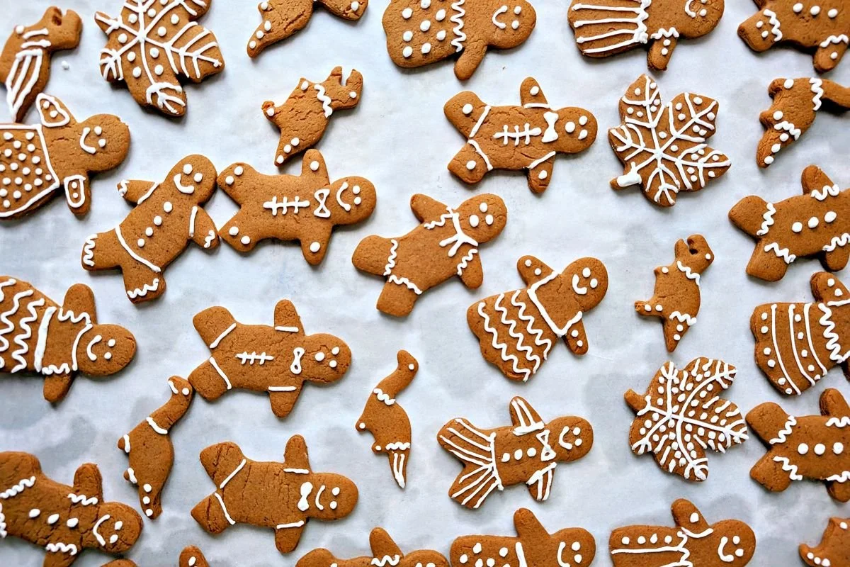 Gingerbread people and dinosaur cookies decorated with white royal icing on parchment paper