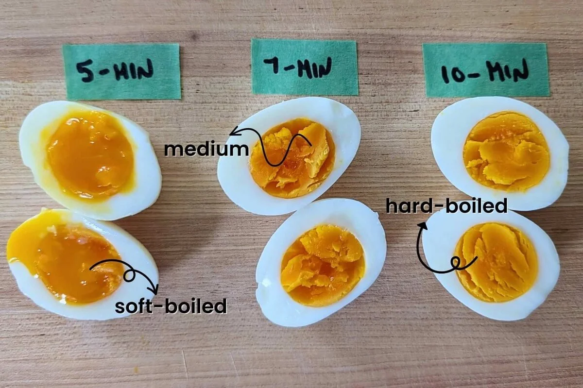 Boiled eggs cooked in a kettle on a wooden cutting board showing three different donenesses: soft-boiled, medium-boiled, and hard-boiled eggs