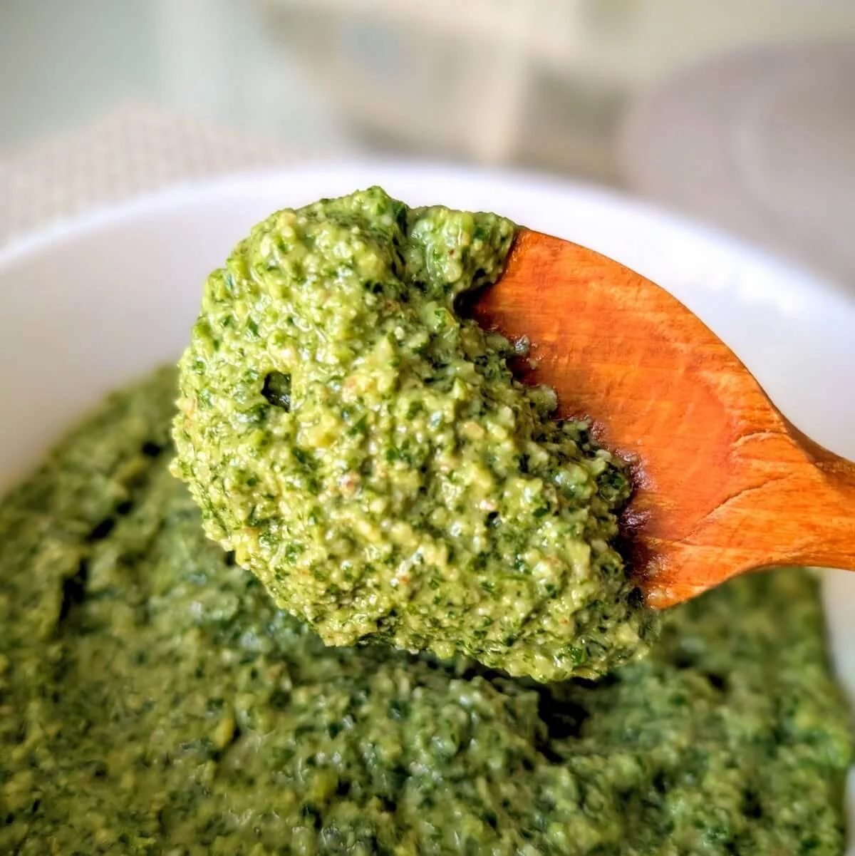 Homemade arugula basil walnut pesto on wooden spoon over a bowl