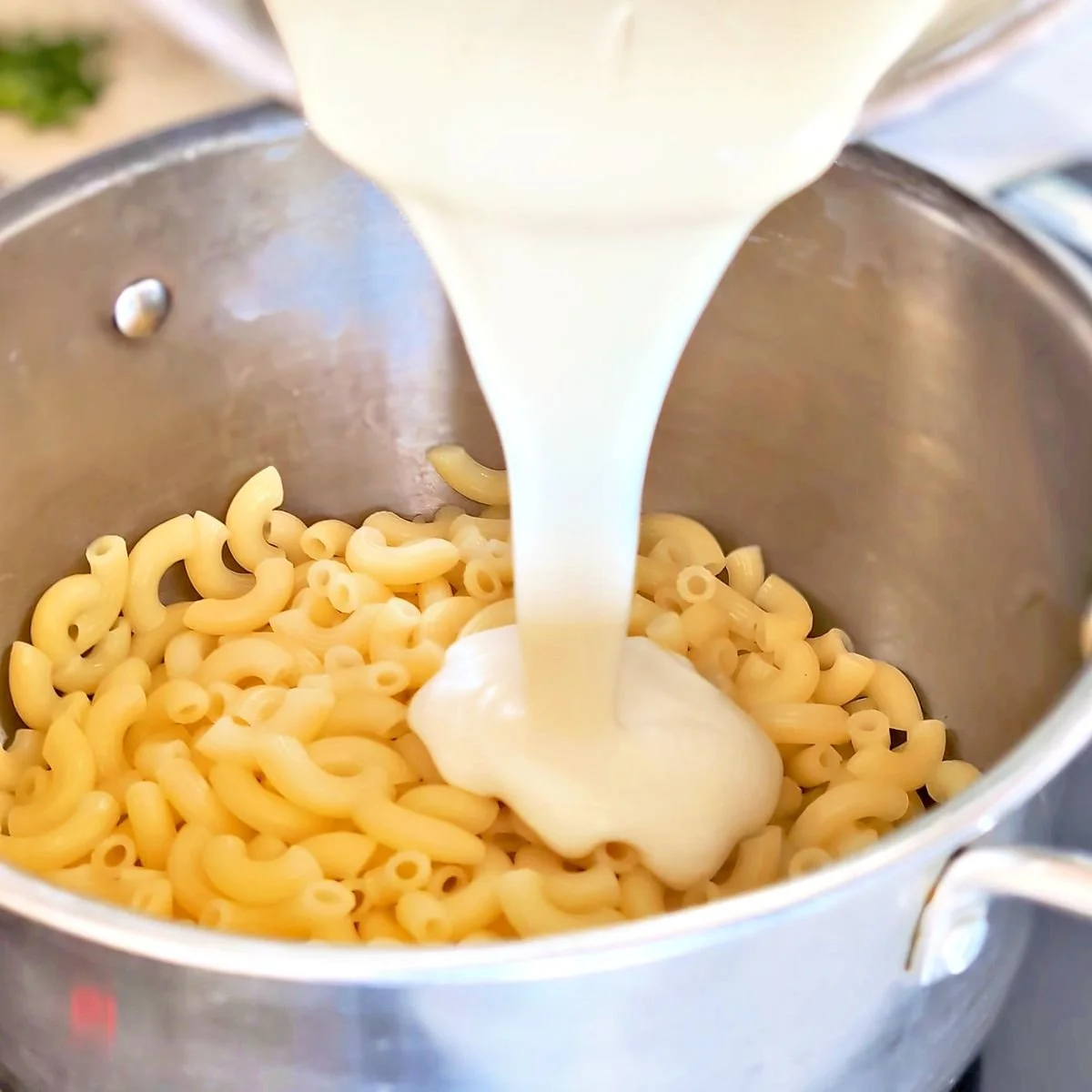 Mornay sauce pouring over cooked macaroni in a pot