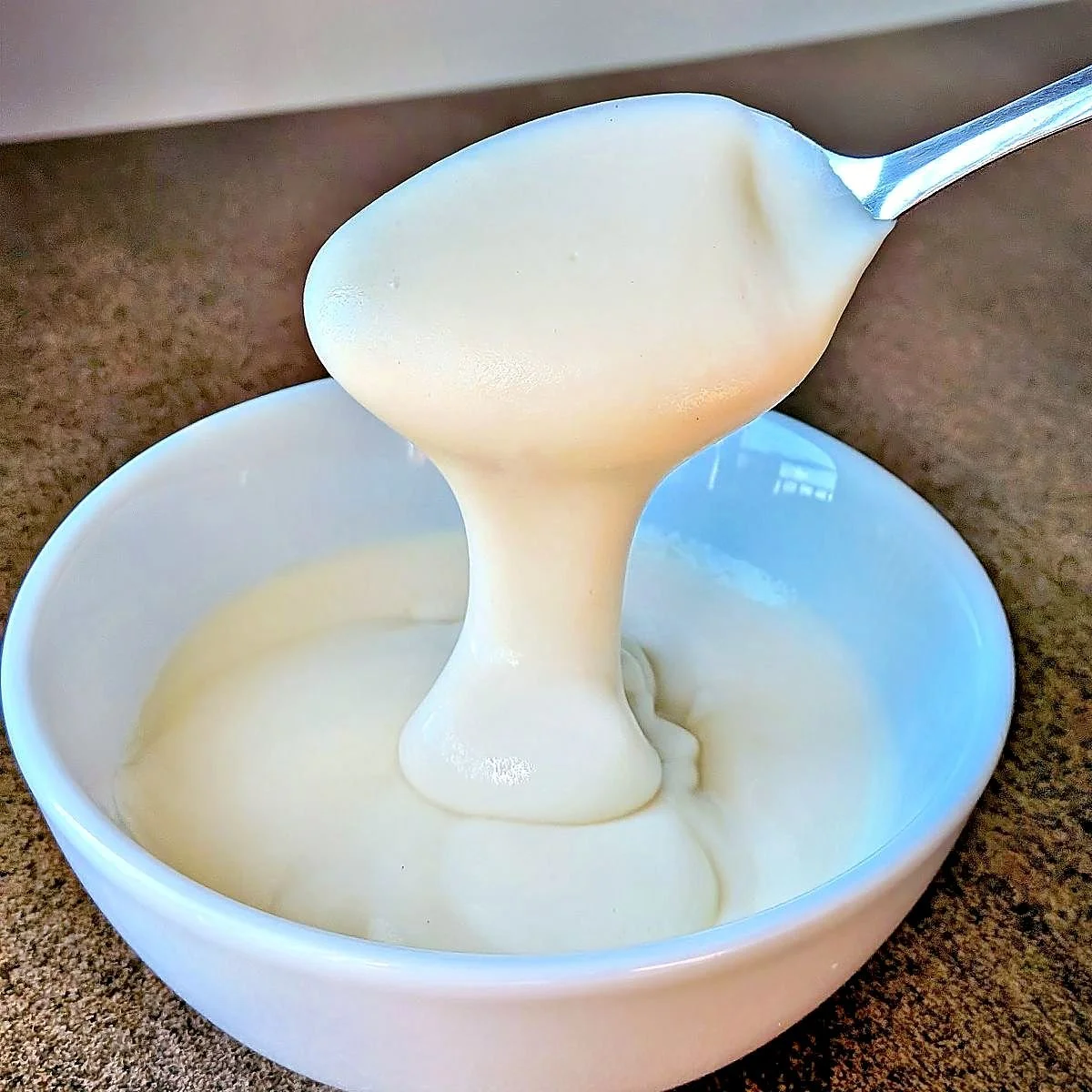 Homemade mornay sauce dripping from a spoon into a white bowl