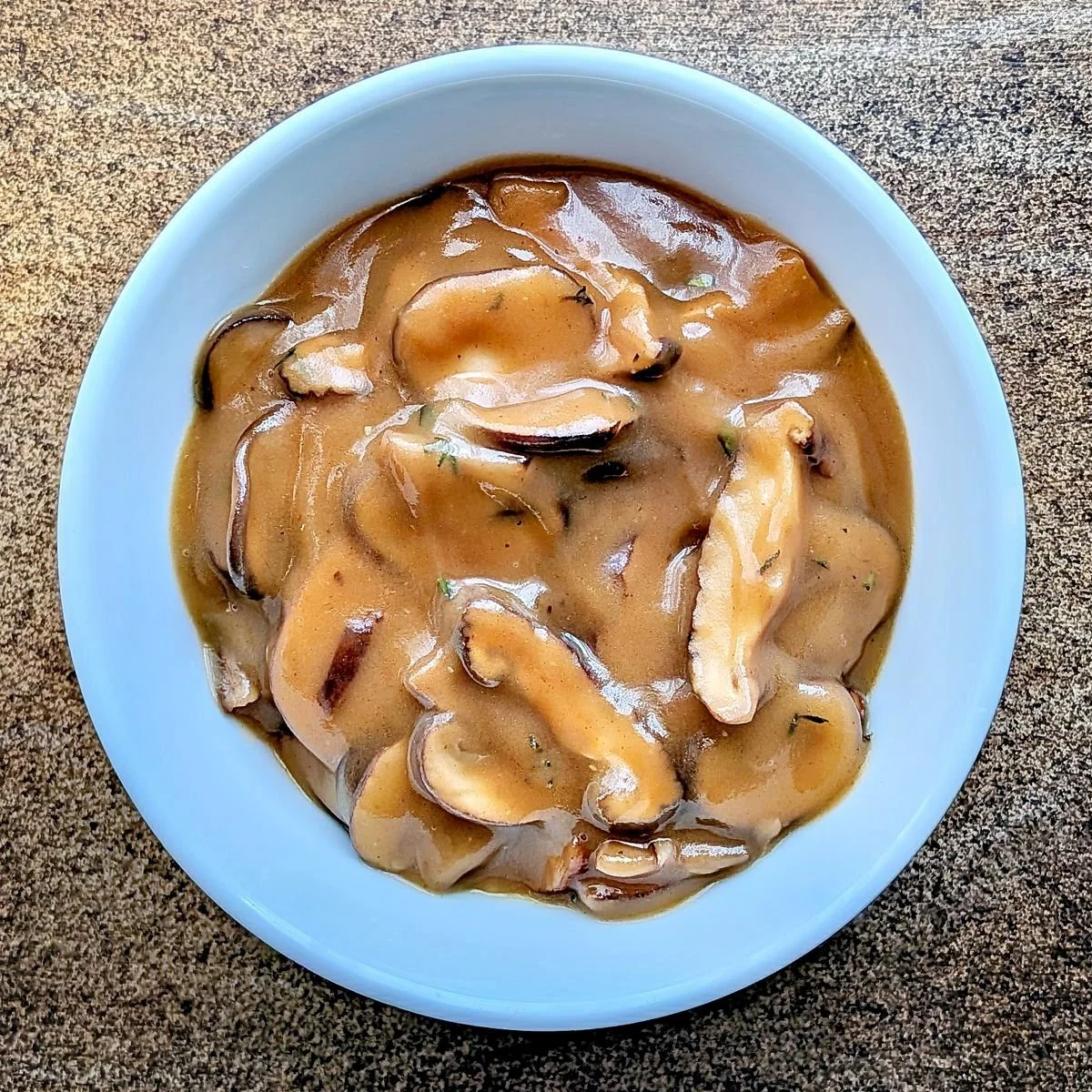 Vegetarian mushroom gravy with browned cremini mushrooms and shiitakes in a white bowl