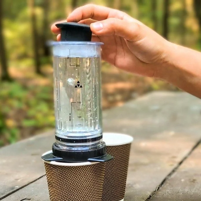 Hand placing the doser on top of a Delter Coffee Press before brewing coffee at a campsite.