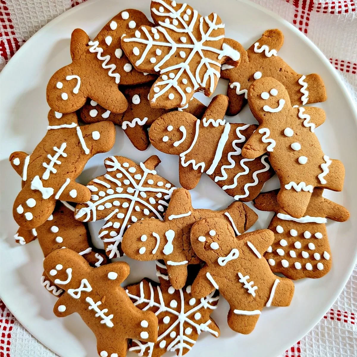 Decorated gingerbread cookies with white royal icing on a plate beside a red-and-white checkered cloth