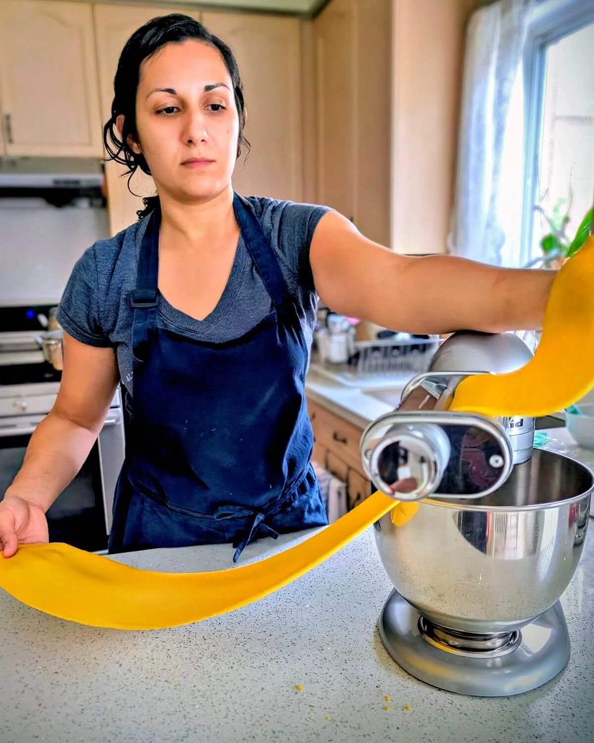 Chef Reem rolling fresh egg pasta dough through a pasta machine in her home kitchen