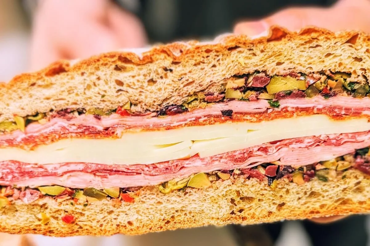 Layered muffaletta sandwich with olive salad, Italian meats, and provolone cheese on crusty round bread, ready to be sliced for a Christmas appetizer