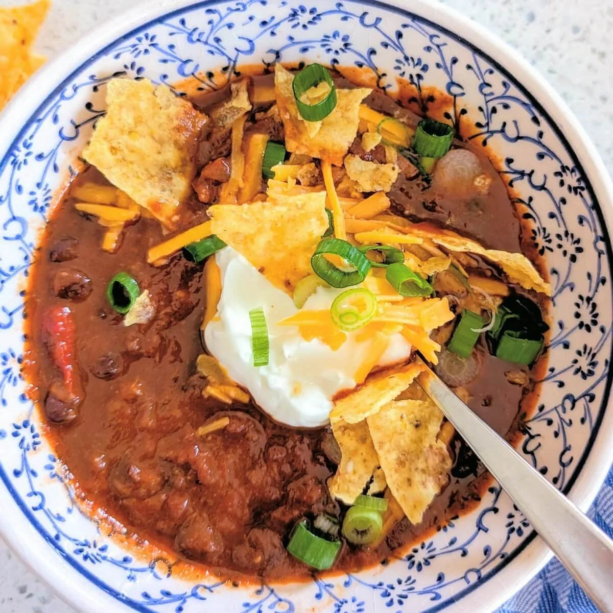 Chili con carne with beef chunks garnished with cheddar, scallions, and sour cream