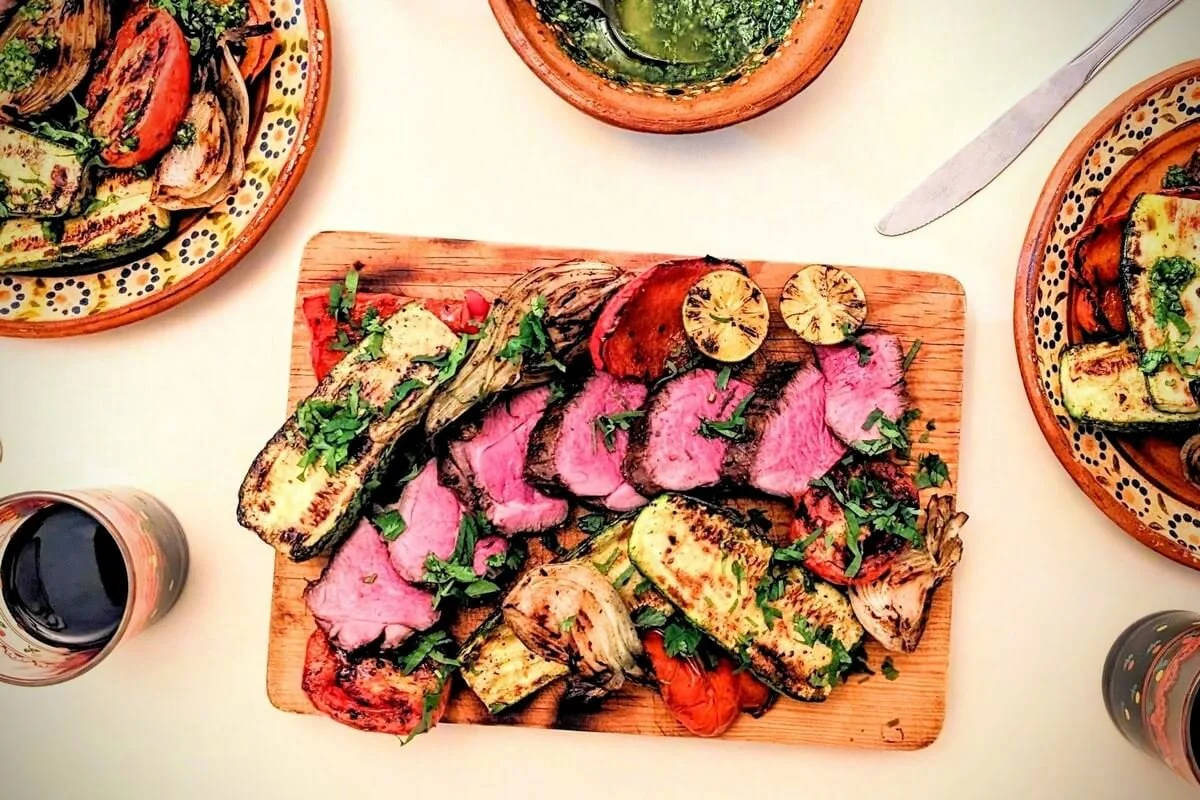 Middle Eastern dinner spread with grilled lamb, charred vegetables, zhoug sauce, and fresh herbs