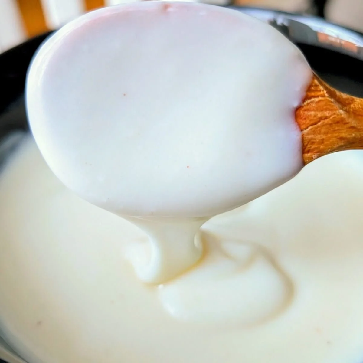 Creamy bechamel sauce dripping smoothly from a wooden spoon