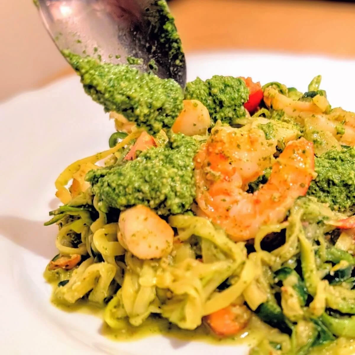 Spoon dolloping arugula and walnut pesto over zucchini noodles with shrimp and scallops on plate
