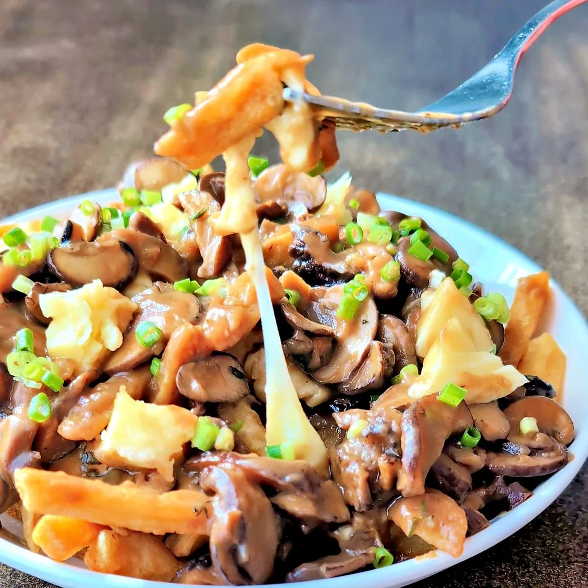 Fork lifting a bite of poutine with stretchy cheese curds and mushroom gravy
