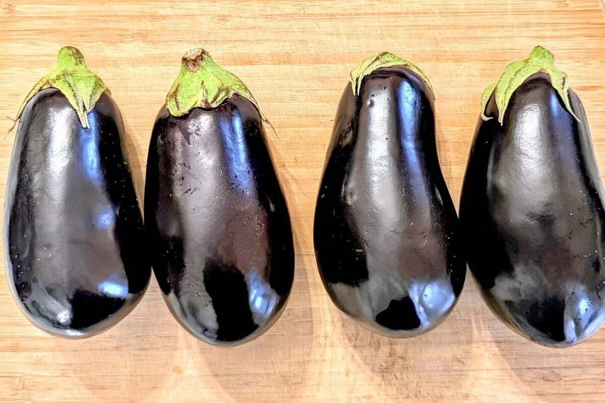 Four Italian eggplants lined up on a cutting board before being prepped for Iraqi eggplant stew