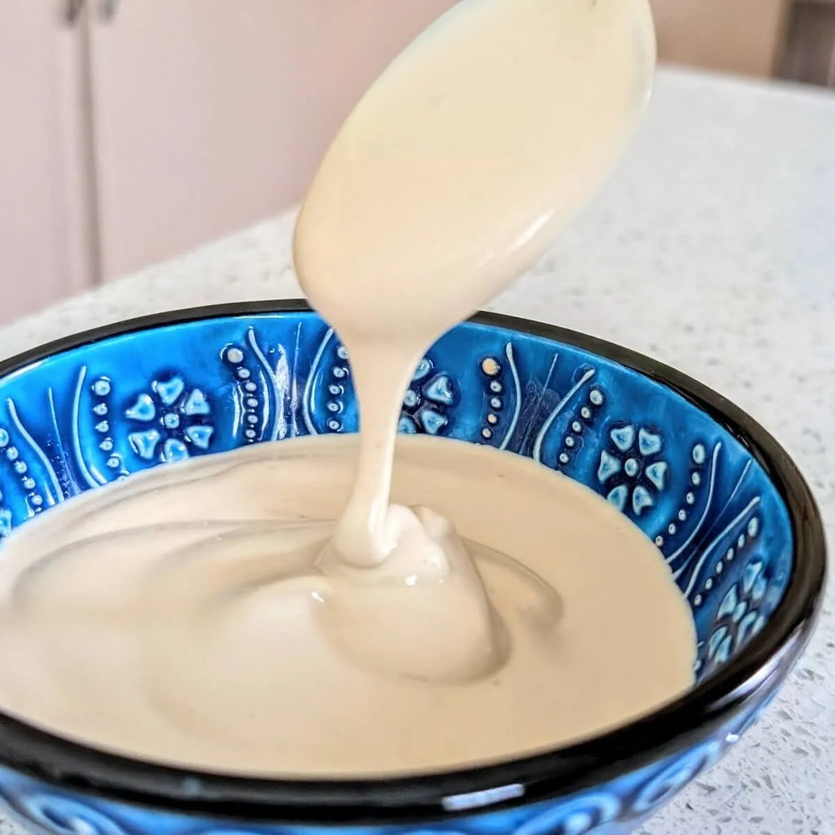 Homemade lemon tahini sauce drizzling off of a spoon into a blue bowl