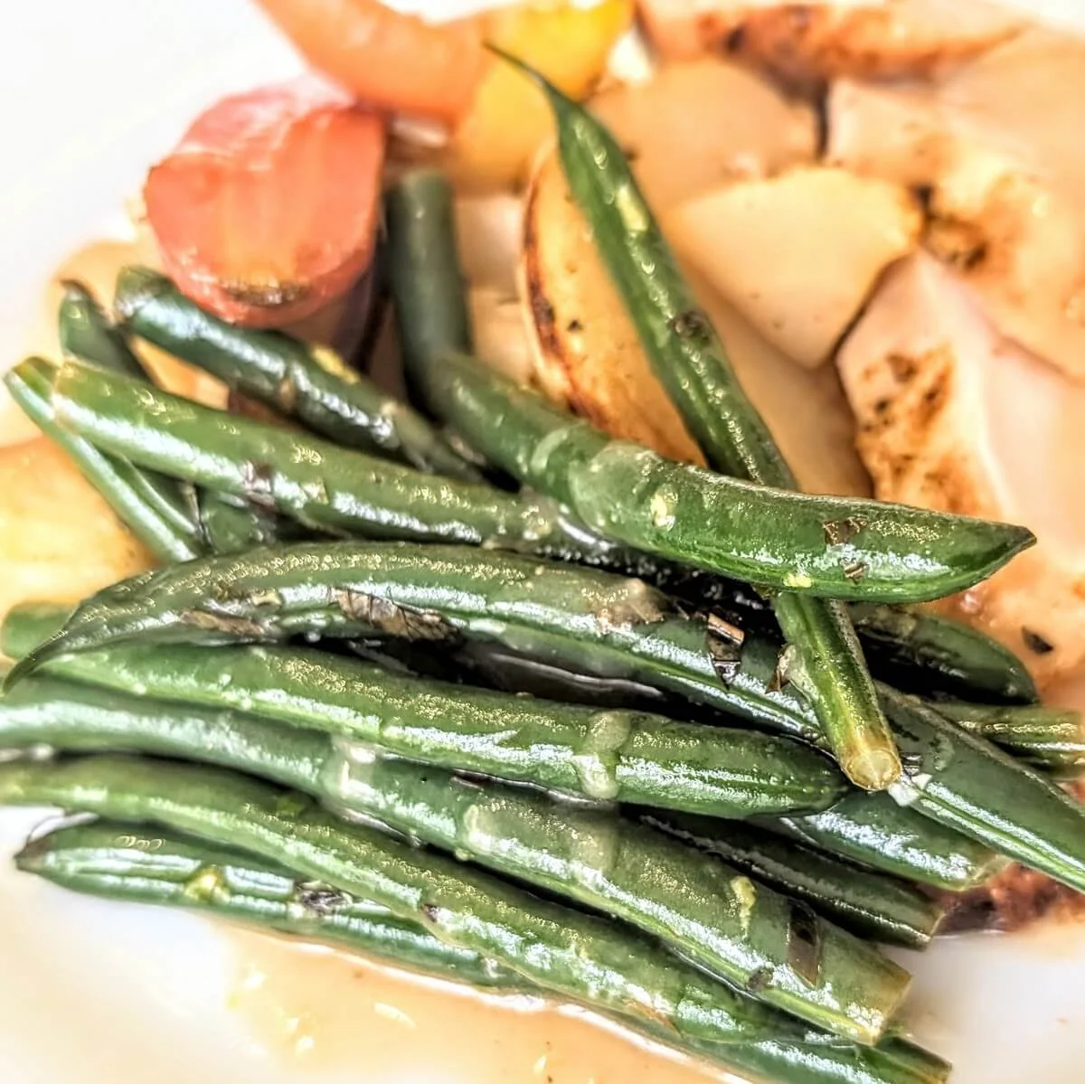 Marinated green beans with herbs and lemon zest on a plate with roast turkey, gravy, and vegetables for a holiday dinner feast