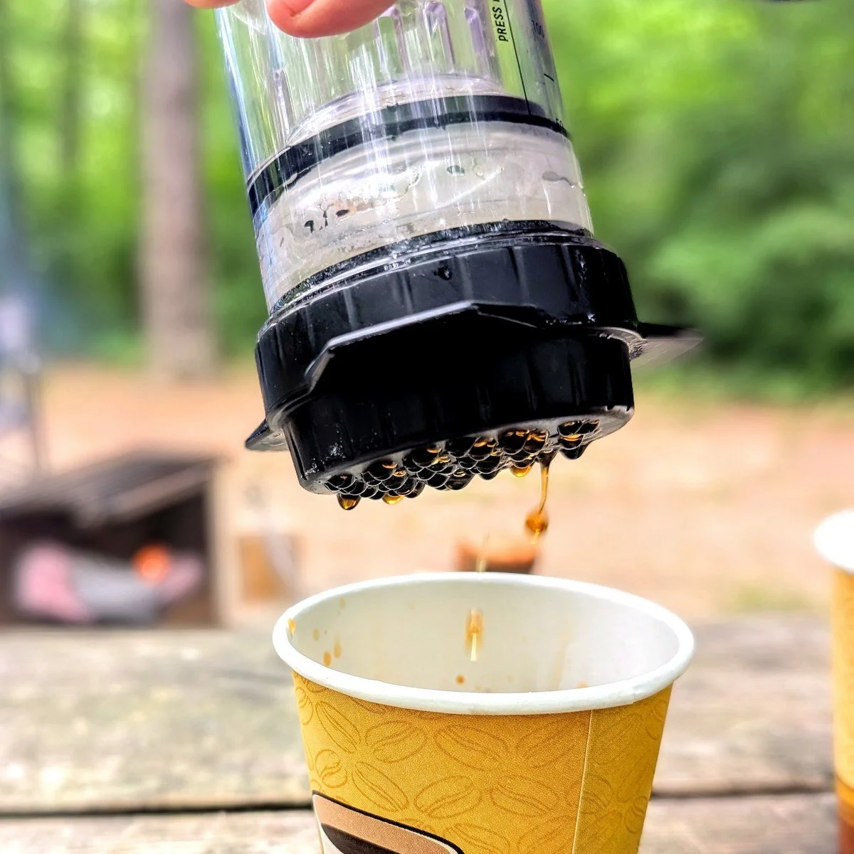 Closeup of coffee dripping out of a Delter Coffee Press into a paper cup at a campsite