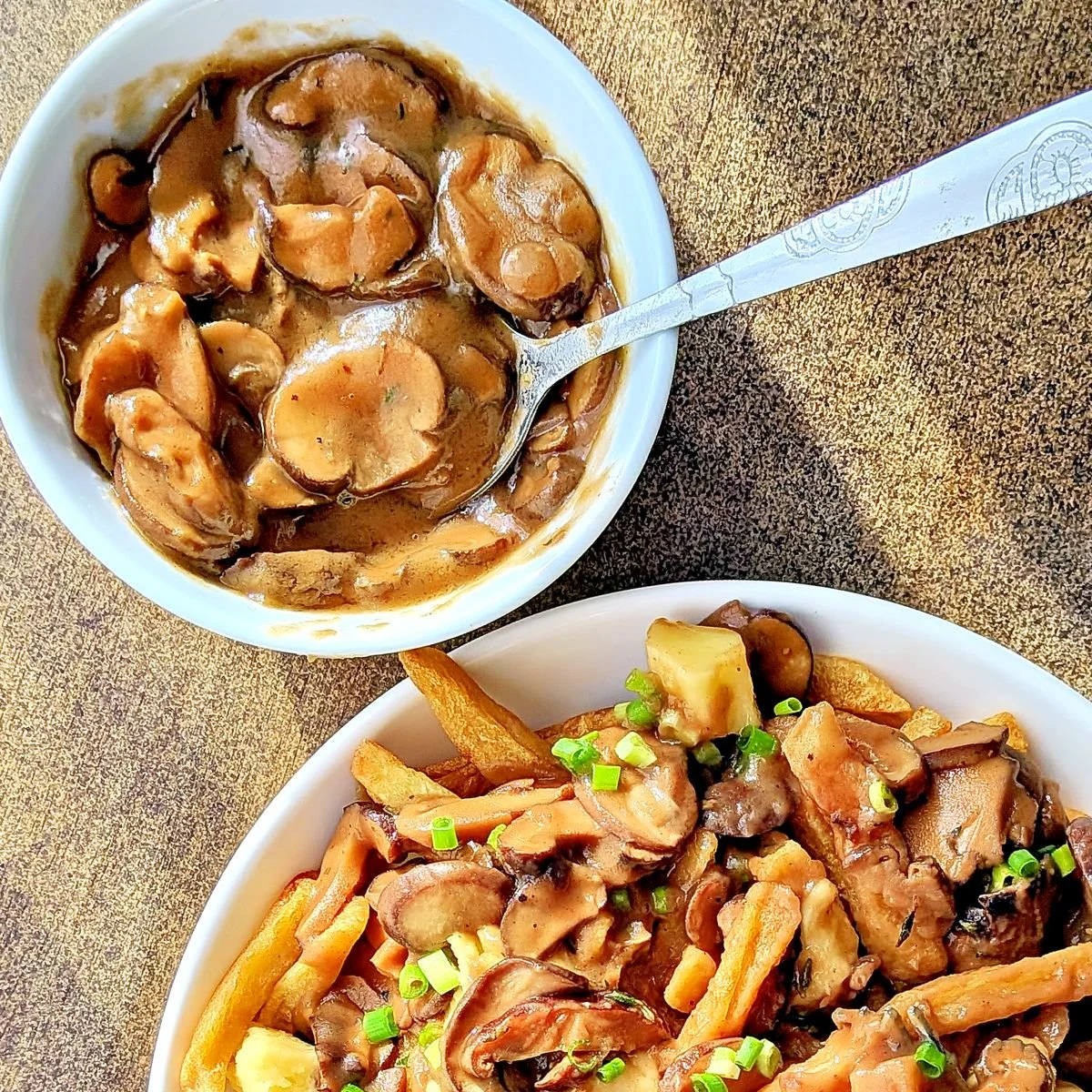 Bowl of mushroom gravy next to poutine with fries, cheese curds, and chives