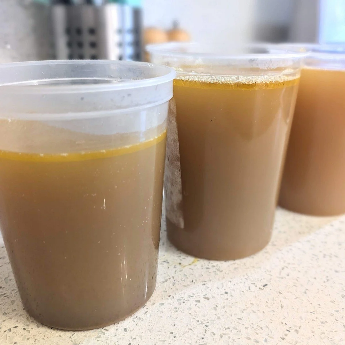 Three 1-liter containers with homemade chicken broth made with vegetable scraps and rotisserie chicken carcass