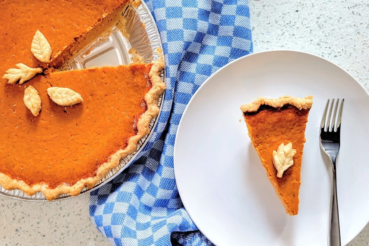 Fully chilled pumpkin pie topped with decorative pie crust leaves with a slice served on a plate